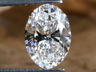 Close-up of a loos oval diamond at Shapiro Diamonds in Dallas held between two tweezers against a blurred background