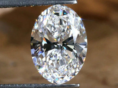 Oval-shaped diamond held between tweezers against a brown background